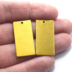 May include: Two gold-colored metal rectangular tags with a hole at the top. The tags are smooth and have a slightly textured surface.