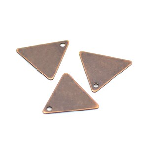 Puede incluir: Tres encantos triangulares de cobre antiguo con un agujero en la parte superior para colgar.
