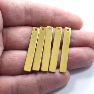 May include: Six gold-colored metal bar pendants with a hole at the top. The bars are flat and rectangular.