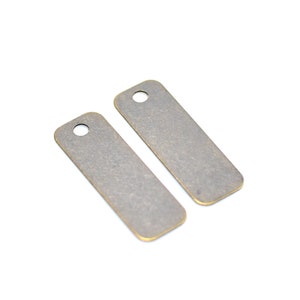May include: Two antique brass rectangular tags with a hole at the top. The tags are blank and have a rough, textured surface.