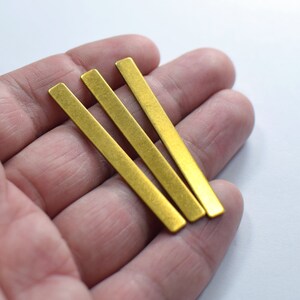 Può includere: Tre barre di metallo dorate, lunghe circa 5 cm, sono tenute in una mano. Le barre sono lisce e hanno una superficie leggermente ruvida.