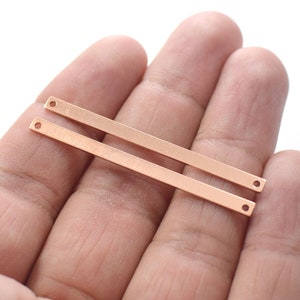 Pode incluir: Dois conectores de barra de metal de cor ouro rosa com furos em cada extremidade. As barras são planas e lisas.