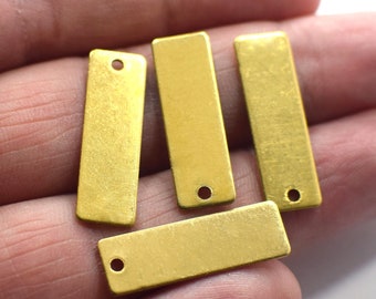 May include: Four small, rectangular, gold-colored metal charms with a hole at one end. The charms are arranged in a close-up shot, showcasing their simple, yet elegant design. These charms are ideal for jewelry making or other craft projects.