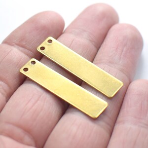 Pode incluir: Duas etiquetas retangulares de metal de cor dourada com dois furos cada. As etiquetas estão em branco e prontas para serem personalizadas.