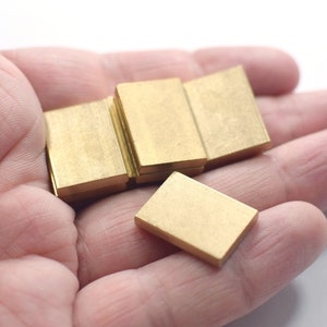 Puede incluir: Una pila de cinco pequeños bloques rectangulares de latón. Los bloques son lisos y tienen un color dorado.