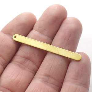 Op de afbeelding: Een gouden metalen staaf met een klein gaatje aan het ene uiteinde. De staaf is ongeveer 5 cm lang en 6 mm breed.