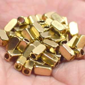 May include: A pile of gold-coloured metal beads, each bead is rectangular with rounded edges and has a hole through the centre.