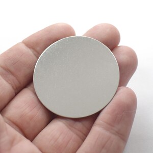 May include: A silver round disc with a smooth, shiny surface.