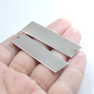 May include: Two silver rectangular metal blanks with a hole in the top. The blanks are smooth and shiny.