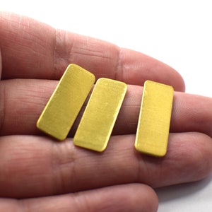 May include: Three gold-coloured rectangular metal pieces, possibly for jewellery making, are held in a hand.