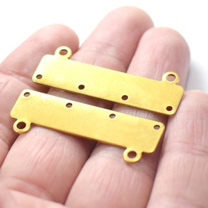 Pode incluir: Duas peças de conexão de metal dourado com quatro furos e dois laços em cada peça.