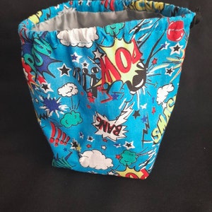 K&ouml;nnte beinhalten: Eine blaue Kordeltasche mit einem Comic-Druck mit W&ouml;rtern wie "Pow!" und "Bang!" und Sternen.