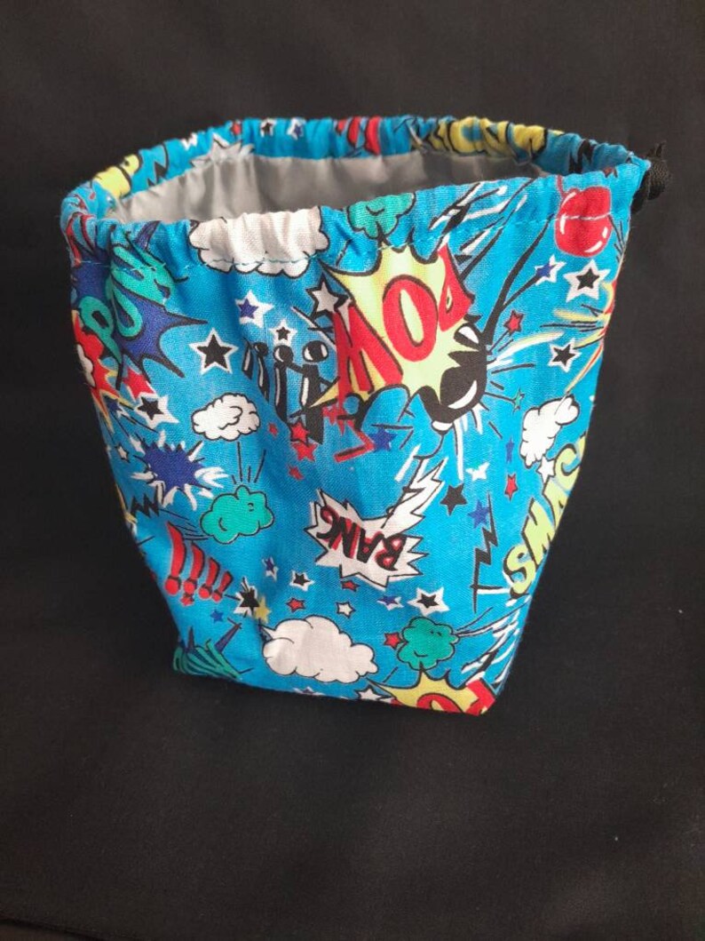 K&ouml;nnte beinhalten: Eine blaue Kordeltasche mit einem Comic-Druck mit W&ouml;rtern wie "Pow!" und "Bang!" und Sternen.
