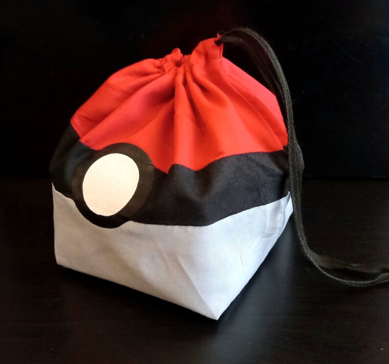 K&ouml;nnte beinhalten: Rote, schwarze und wei&szlig;e Kordeltasche mit einem Pokeball-Design.