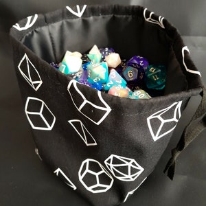 K&ouml;nnte beinhalten: Schwarzer Stoff-W&uuml;rfelbeutel mit wei&szlig;en geometrischen Mustern. Der Beutel ist mit bunten W&uuml;rfeln gef&uuml;llt.