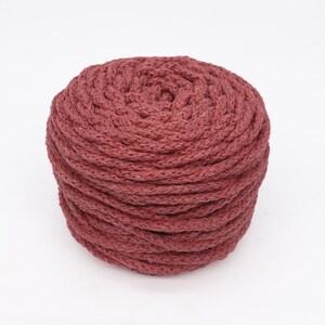 May include: A close-up of a spool of thick, red-brown cotton rope. The rope is tightly wound and has a natural, textured look.