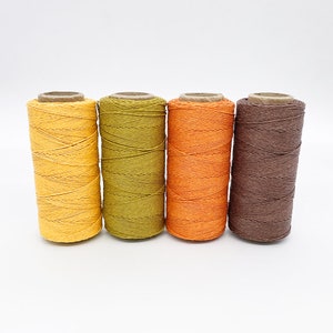 May include: Four spools of cotton twine in shades of yellow, green, orange, and brown.