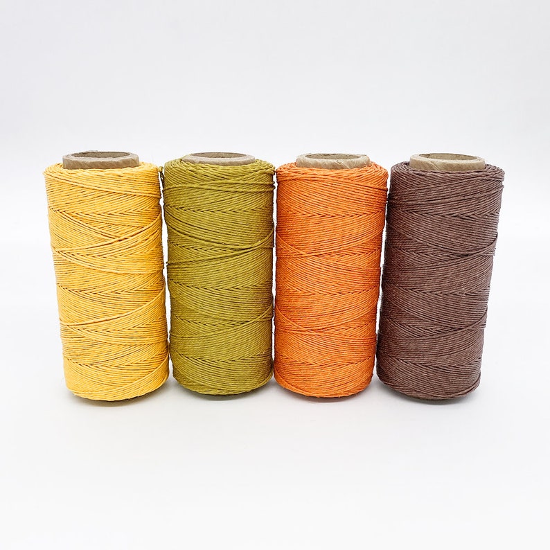 May include: Four spools of cotton twine in shades of yellow, green, orange, and brown.