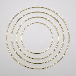 Puede incluir: Conjunto de cuatro aros de metal dorado de diferentes tamaños. Los aros están dispuestos en un patrón de círculo concéntrico.