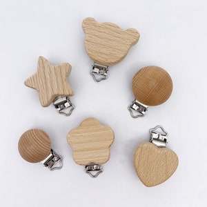 May include: Five wooden baby teethers with metal clips. The teethers are shaped like a star, a bear, a circle, a flower, and a heart. The teethers are all natural wood color.