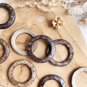 May include: A set of eight wooden rings, some with a natural brown finish and others with a light brown finish. The rings are all different sizes and are arranged in a circle on a wooden surface.