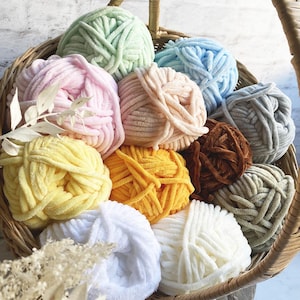 May include: A basket filled with various colors of yarn, including pink, blue, green, yellow, brown, and white. The yarn is soft and fluffy, and it is perfect for knitting or crocheting.