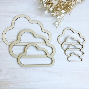 May include: Five wooden cloud shapes of varying sizes, arranged in a descending order from largest to smallest. The clouds are cut out of a light brown wood and have a smooth, unfinished surface.