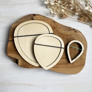 Può includere: Tre modelli di petali di fiori in legno di diverse dimensioni. I modelli sono su una superficie di legno. Il modello più piccolo ha il testo "10 x 7" scritto su di esso.