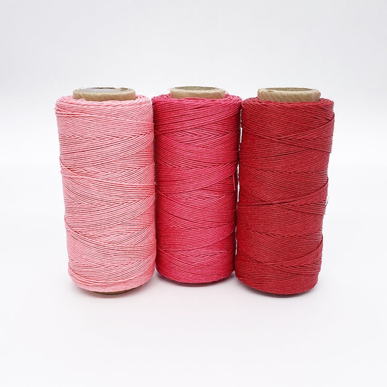 May include: Three spools of pink and red cotton thread. The spools are made of cardboard and have a natural brown color.