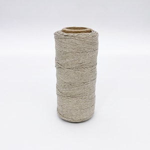May include: A spool of natural beige twine, wound around a cardboard tube.