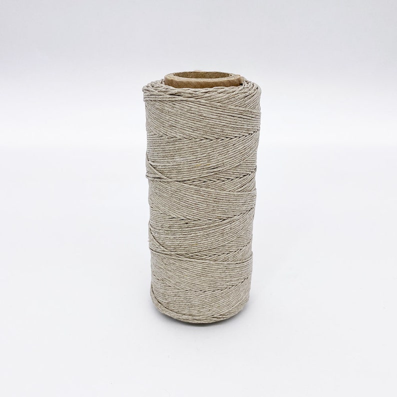 May include: A spool of natural beige twine, wound around a cardboard tube.