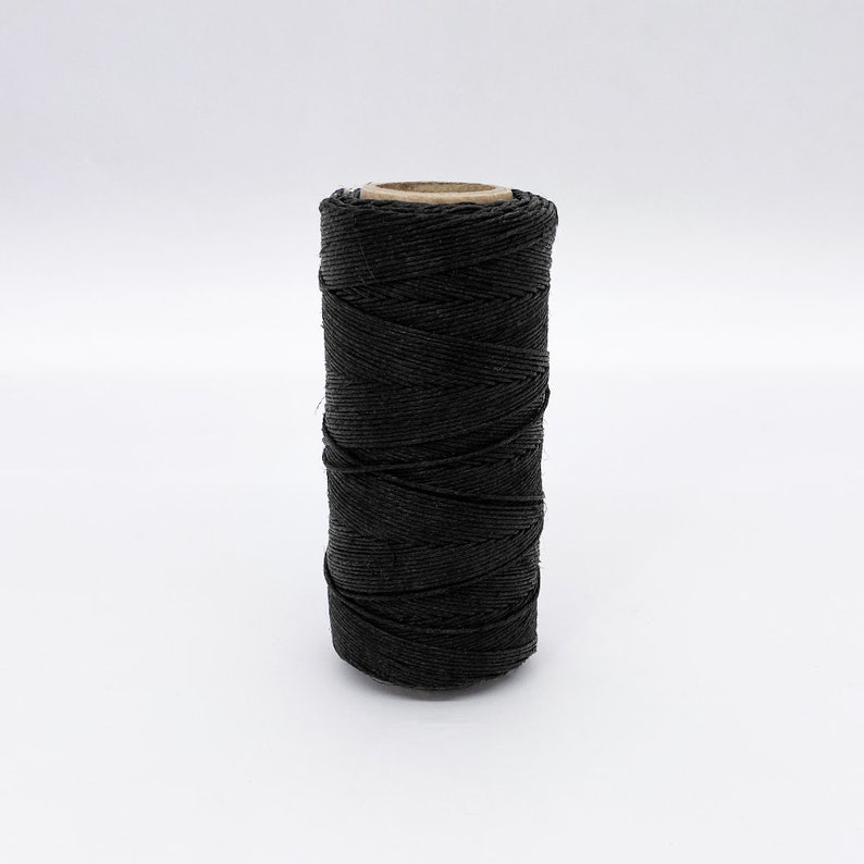 May include: A spool of black waxed linen thread.