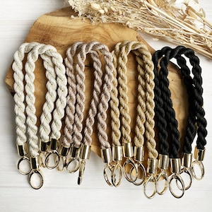 May include: Five different colours of braided rope with gold-toned clasps. The ropes are in shades of white, beige, brown, gold, and black.