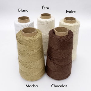 Könnte beinhalten: Fünf Spulen Baumwollgarn in verschiedenen Farben: Weiß, Creme, Beige, Braun und Dunkelbraun. Die Spulen sind mit den Farben beschriftet: Blanc, Écru, Ivoire, Mocha und Chocolat.