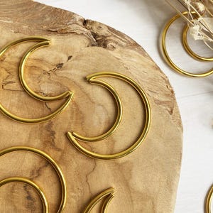 Puede incluir: Un conjunto de cinco formas de media luna de metal dorado sobre una superficie de madera. Las lunas son de diferentes tamaños y están dispuestas en un patrón aleatorio.