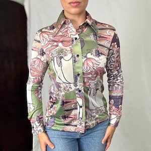 May include: A long-sleeved button-down shirt with a colorful floral pattern in shades of green, pink, and purple. The shirt has a large collar and is made of a silky material. The design features stylized flowers and abstract shapes.