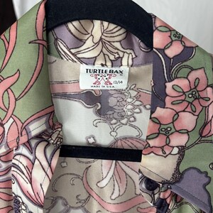May include: A vintage button-down shirt with a floral pattern in shades of pink, green, and purple. The shirt features a collar and a label that reads "TURTLE BAX" and "13/14". Made in the USA.