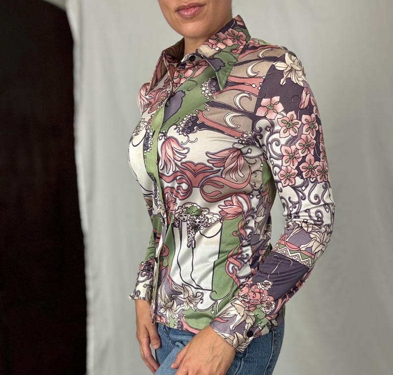 May include: A button-down shirt with a floral pattern in shades of pink, green, and purple. The long-sleeved shirt has a collared neckline and a fitted silhouette. The fabric appears to be a silky material.