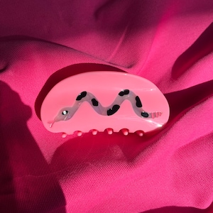 May include: Pink plastic hair claw with a black and white snake design.