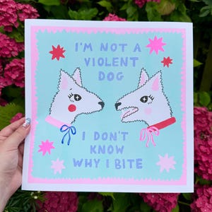 May include: A light blue print with a pink border features two white dogs with red and blue collars. The text reads "I'm not a violent dog. I don't know why I bite."