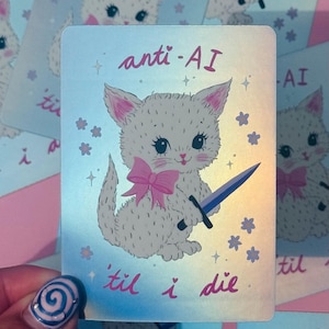 Puede incluir: Una pegatina holográfica rectangular que muestra un gatito blanco con un lazo rosa alrededor del cuello, sosteniendo una espada azul. El texto anti-AI está impreso sobre el gatito y el texto 'til i die debajo, rodeado de pequeñas estrellas moradas.