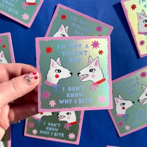 May include: Two white dogs with pink bows are facing each other. The dog on the left has a red circle on its cheek. The dog on the right has its mouth open and is showing its teeth. The text on the sticker reads "I'm not a violent dog. I don't know why I bite."