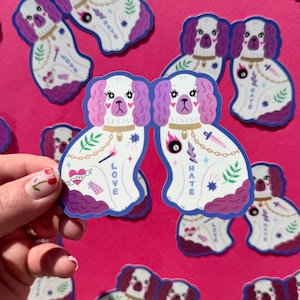 Puede incluir: Dos perros blancos con pelo rizado morado se miran. Llevan cadenas de oro y tienen varios tatuajes, incluyendo un corazón, una estrella, un rayo, una daga, una calavera y una bola de billar. El perro de la izquierda tiene la palabra "LOVE" escrita en su lado y el perro de la derecha tiene la palabra "HATE" escrita en su lado.