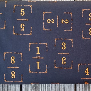 Peut inclure: Tissu noir avec un motif répété de fractions encadrées d'or. Les fractions comprennent 7/2, 5/9, 3/8, 1/1, 5/9, 3/8, 4, 2/2 et 8/8.