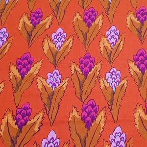 May include: Bright orange fabric with a repeating floral design. The pattern showcases stylized flowers in shades of purple and pink, set against large, brown leaves. The fabric is rolled at the top, and a black pen rests on the fabric.