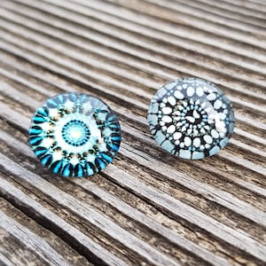 Puede incluir: Dos cabujones redondos de vidrio con diseños de mandalas azules y blancos. Los cabujones están sobre una superficie de madera.