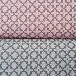 May include: Close-up of two fabric samples. The top sample is a dusty rose color with a repeating gray geometric pattern. The bottom sample is teal with a similar gray geometric pattern. The fabric has a textured appearance.