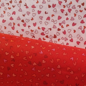 May include: Two pieces of fabric with a repeating pattern of small red hearts on a white background. The top piece of fabric is white with pink hearts, and the bottom piece of fabric is red with red hearts.