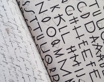 May include: Two fabric swatches with different patterns. One features black letters and geometric shapes on a light background. The other has handwritten script in black ink on a light background. Both fabrics are folded.