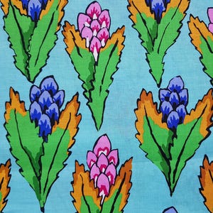 May include: Floral fabric with a repeating pattern of stylized flowers in pink, blue, green, and orange on a light blue background. A black pen is placed on the fabric for scale.